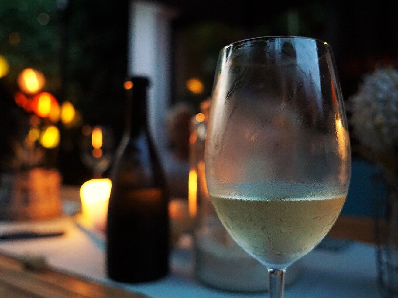 Gekühltes Glas Weißwein auf einem Tisch bei stimmungsvoller Beleuchtung und Kerzenschein.