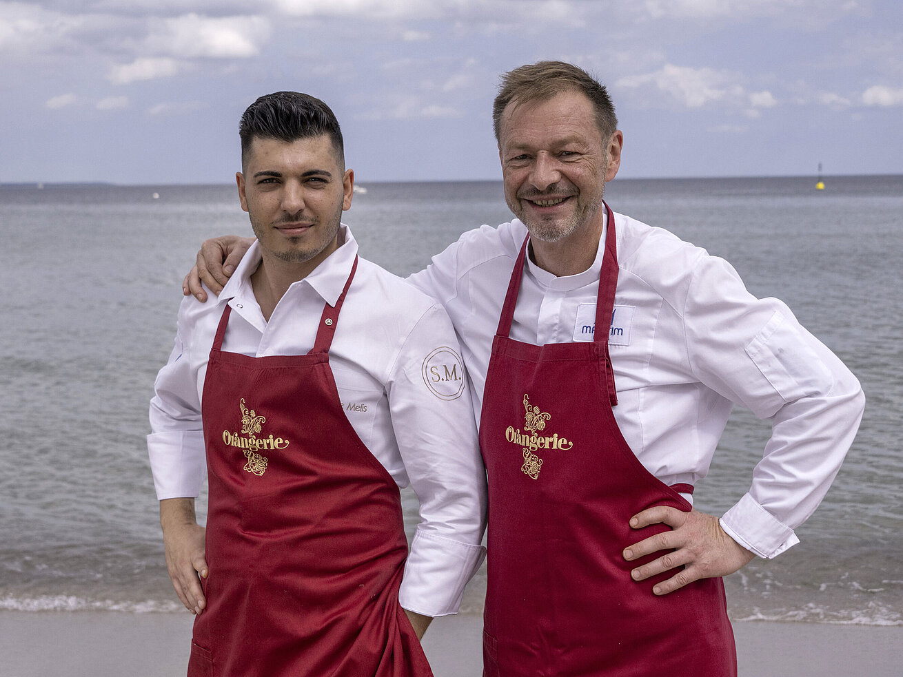 Küchenchefs Thomas Lemke und Simone Melis Küchenchefs Simone Melis und Thomas Lemke mit roten Schürzen am Meer vor dem Maritim Hotel Timmendorfer Strand.
