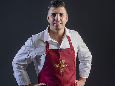 Küchenchef Simone Melis in der Orangerie im Maritim Hotel Timmendorfer Strand, in weißer Kochjacke und roter Schürze mit Logo