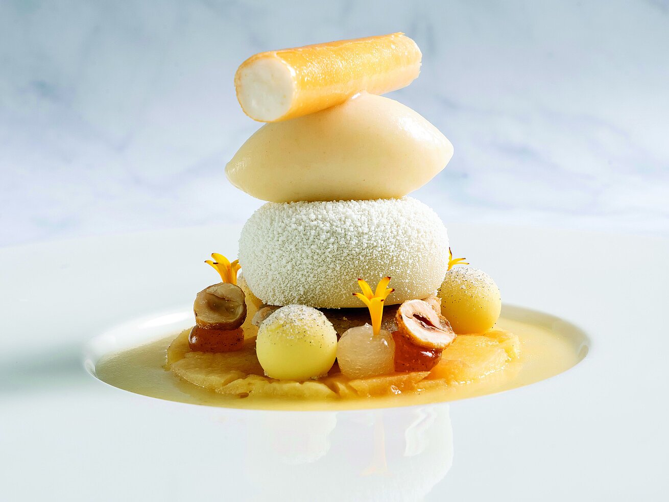 Gourmetdessert mit Eis, Nüssen und Blüten, kunstvoll auf weißem Teller angerichtet