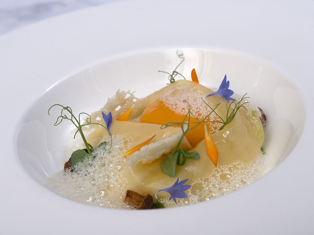 Ein Teller mit Ravioli in einer cremigen Sauce, garniert mit essbaren Blüten.