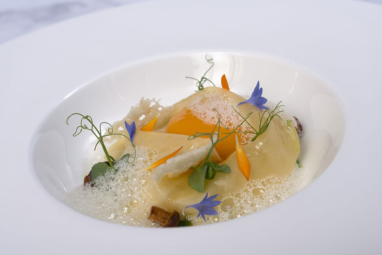 Ein Teller mit Ravioli in einer cremigen Sauce, garniert mit essbaren Blüten.