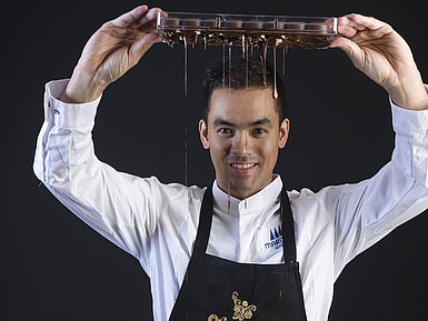 Taro Bünemann, Chef Pâtissier der Orangerie im Maritim Timmendorfer Strand, hält ein Tablett, von dem Schokolade tropft.