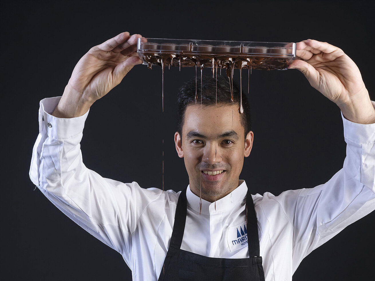 Chef Pâtissier Taro Bünemann Taro Bünemann, Chef Pâtissier der Orangerie im Maritim Timmendorfer Strand, hält ein Tablett, von dem Schokolade tropft.