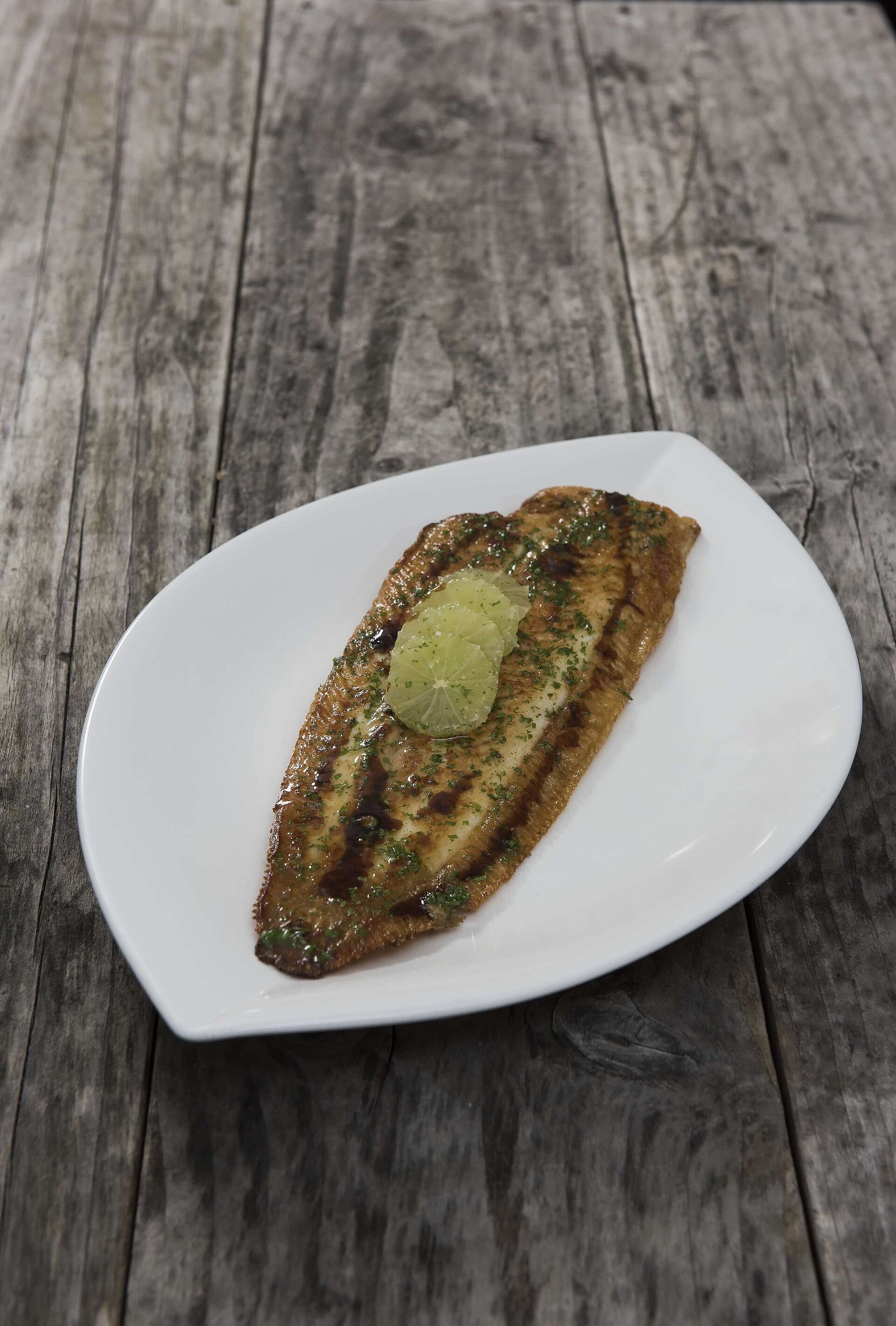 Fischgericht Knusprig gebratener Fisch mit Kräutern und Zitronenscheiben auf weißem Teller in der Orangerie Timmendorfer Strand.