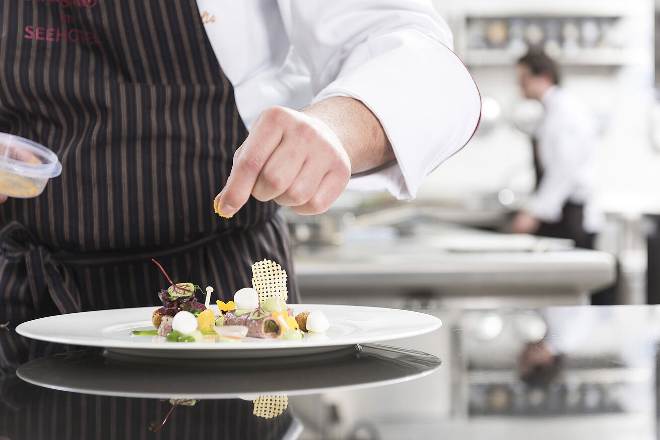 Koch richtet ein Gourmetgericht mit Gemüse, Kräutern und kunstvollen Elementen in der Orangerie an.
